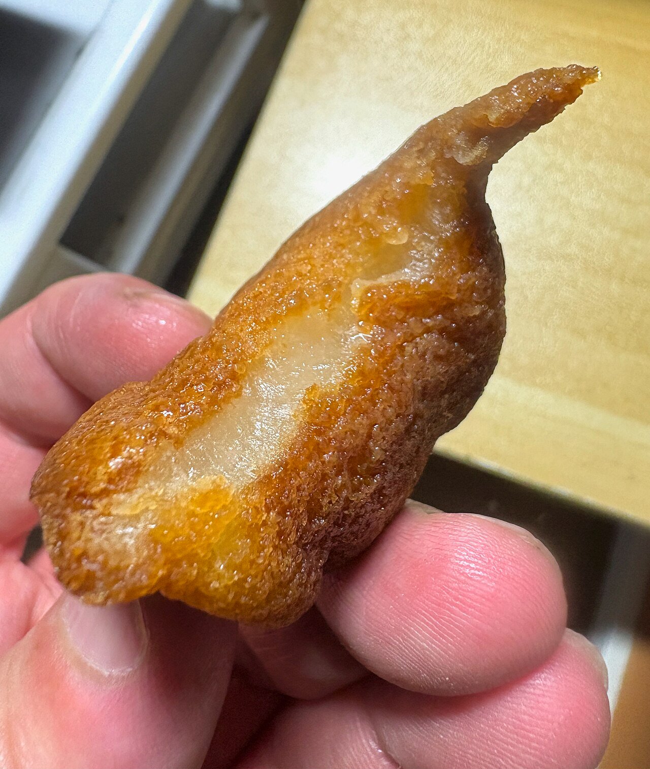 Hand holding a golden butter tteok-style rice cake snack