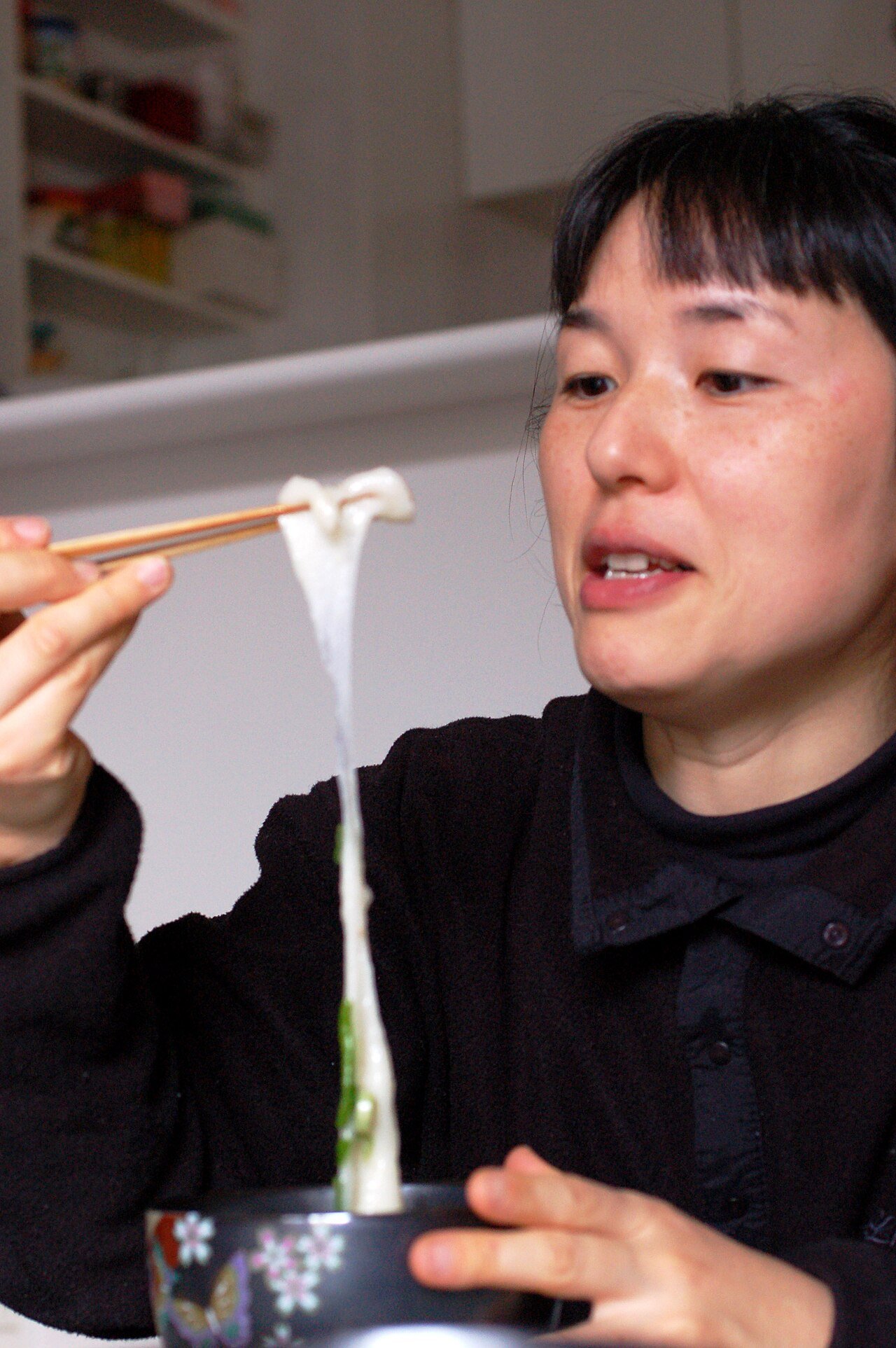 Young woman eating stretchy chewy rice cake with chopsticks