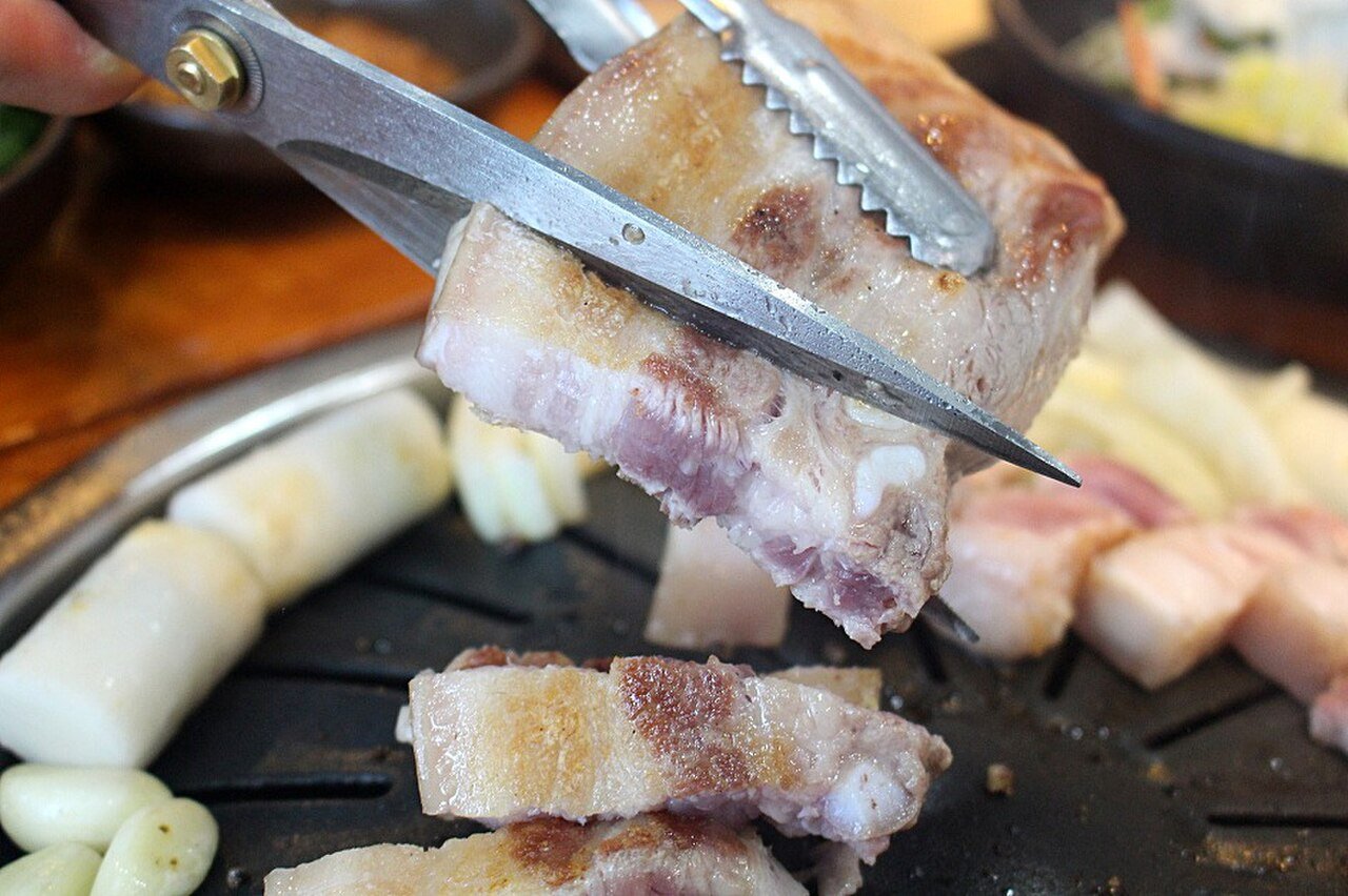 Cutting grilled samgyeopsal pork belly with scissors on a cast-iron grill in a Korean restaurant